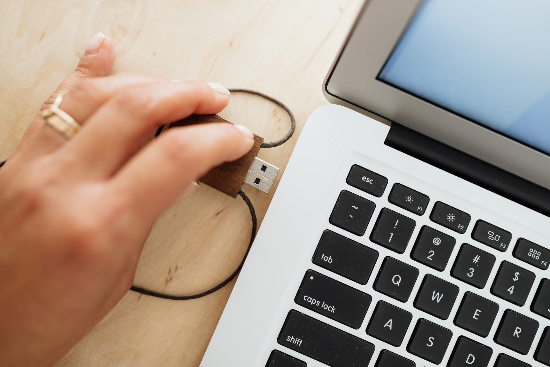 Main qui branche une clé USB en bois sur un ordinateur portable, sur un bureau en bois