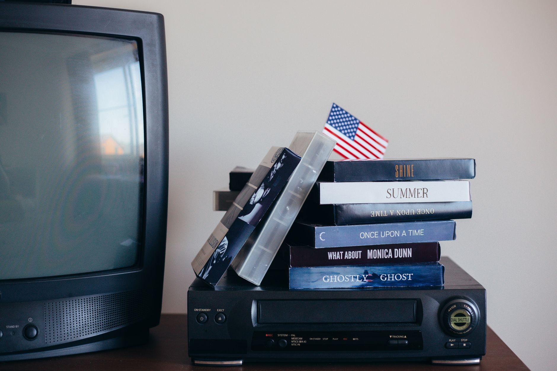 Pile de cassettes VHS posée sur un vieux magnétoscope, devant une télévision, dans une ambiance nostalgique de salon familial