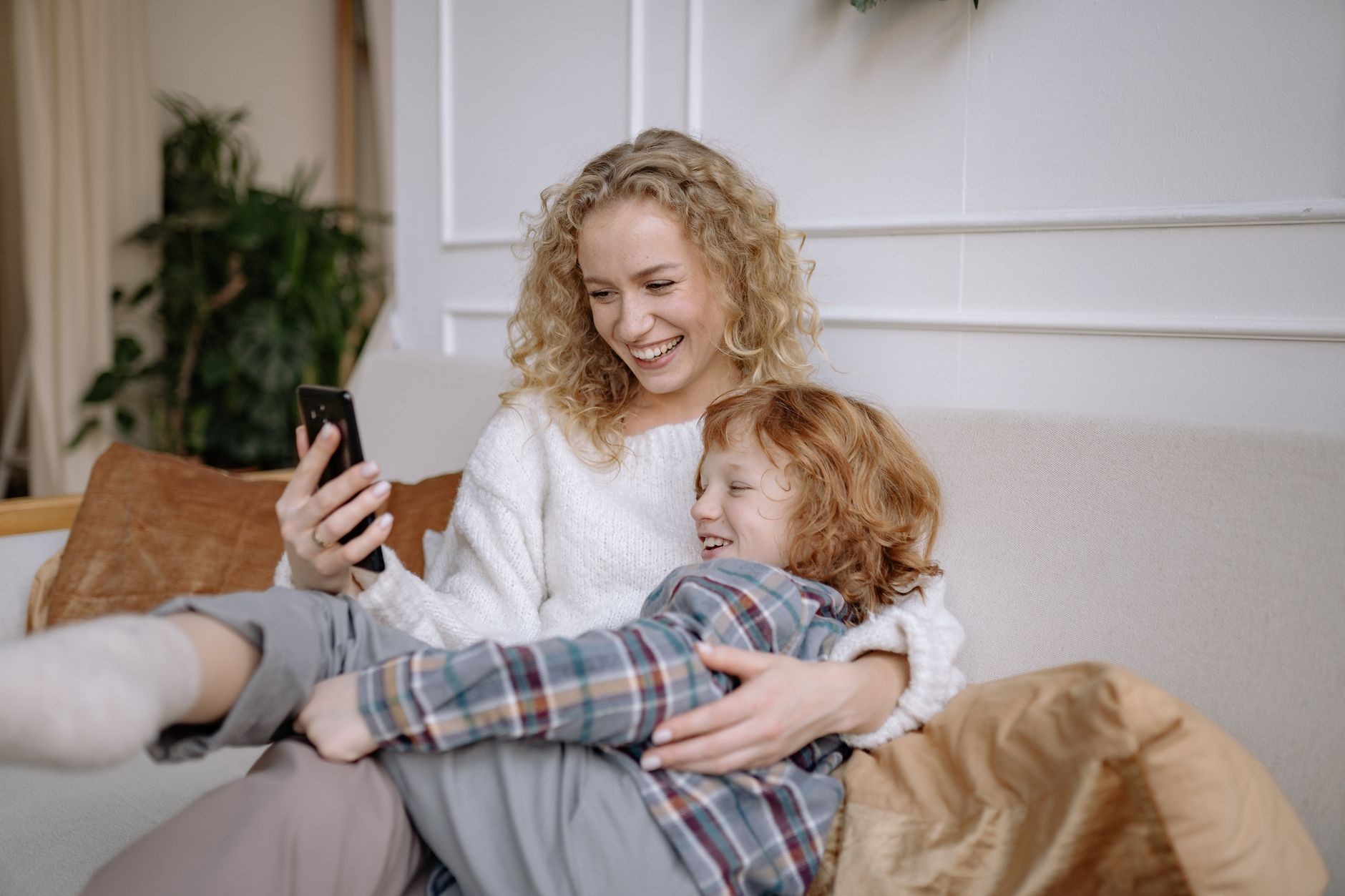 Une mère et son fils souriants regardent ensemble des photos sur un smartphone, installés confortablement sur un canapé