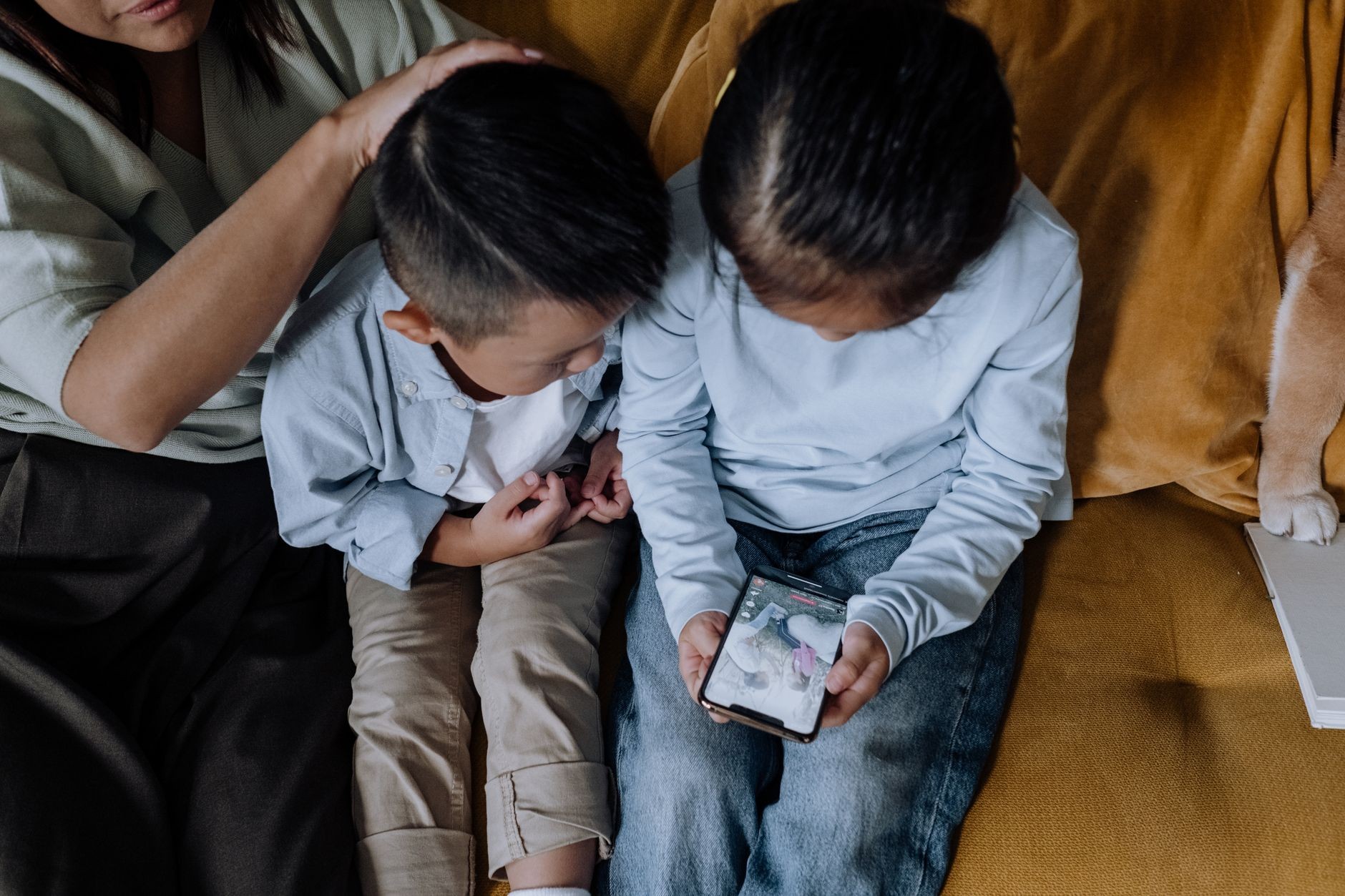 Deux enfants regardent ensemble des photos de famille sur un smartphone, installés sur un canapé